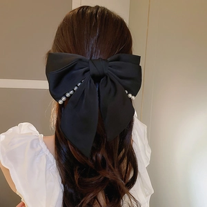 Détail d'une élégante pince à cheveux noeud en soie noire ornée de perles blanches