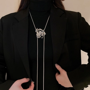 Detail of a large silver metallic flower pendant on a sleek snake chain over black fabric