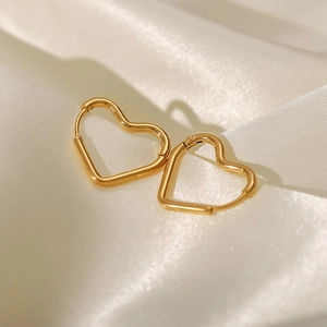 Detail of gold heart-shaped hoop earrings on white satin fabric with metallic texture