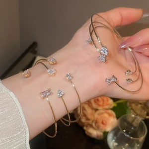 Close-up of three gold open bracelets with star, heart, and square zircon stones on wrist