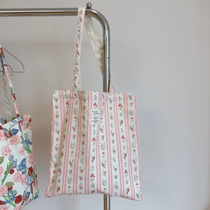 Detailed view of floral canvas tote bag with red stripes and white woven label