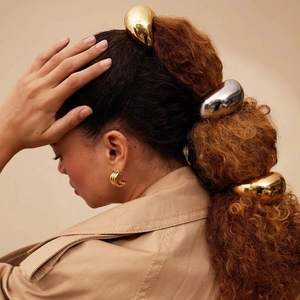 Detail of minimalist metallic gold and silver hair rings worn on a sleek ponytail