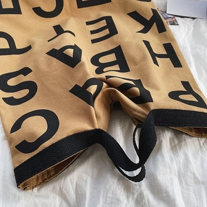 Detail of camel canvas tote with bold black alphabet prints and woven handles