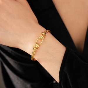 Close-up of gold-plated knotted cuff bracelet worn by a model on a dark background