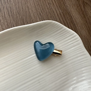Macro detail of jelly blue heart hair clip with gold metal base on ceramic tray