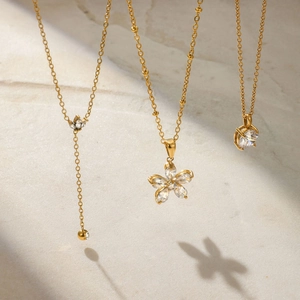 Three gold stainless steel necklaces with zircon pendants on a marble background