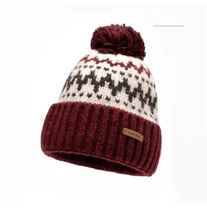 Detail of claret knit beanie featuring a fluffy pompom and branded leather patch