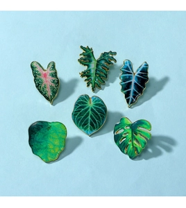 Detailed flat lay of six colorful enamel tropical leaf pins with elegant gold metal edges