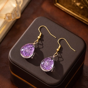 Detailed close-up of purple dried flower teardrop earrings on a vintage jewelry box