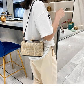 Detail of woven straw shoulder bag with black PU strap and gold buckle worn by model