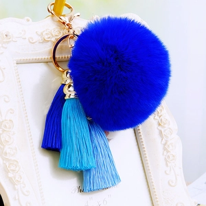 Detail of blue faux fur pompom and gradient silk tassels on golden metal keychain