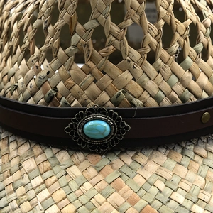 Detail of straw cowboy hat with leather band and turquoise stone metal buckle