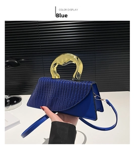 Detail of dark blue crocodile pattern flap bag with unique gold metal handle and strap