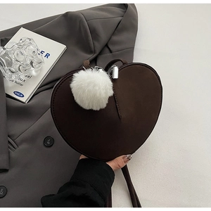 Detail einer braunen herzförmigen Wildledertasche mit weißem Plüsch-Pompon-Anhänger