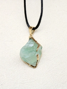 Détail d'un pendentif en pierre naturelle verte irrégulière avec bords dorés polis
