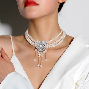 Close-up of triple-layer pearl necklace with heart pendant and tassel on neck