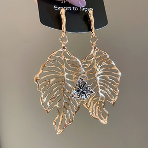 Detailed view of oversized golden hollow leaf earring with silver floral centerpiece accent