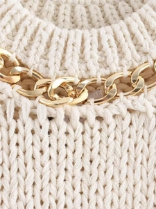 Detail of cream cable knit sweater featuring a decorative gold metal chain neckline