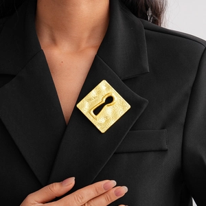 Detail of a hammered gold square brooch with keyhole cutout on a black suit lapel