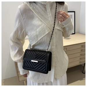 Detail of black crossbody bag featuring V-quilted pattern and elegant metal chain strap