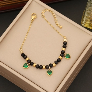 Golden bracelet with emerald green heart charms and beads in a beige jewelry box