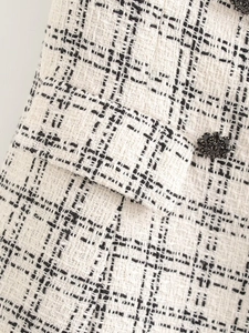 Detailed close-up of black and white tweed fabric featuring a pocket flap and decorative button