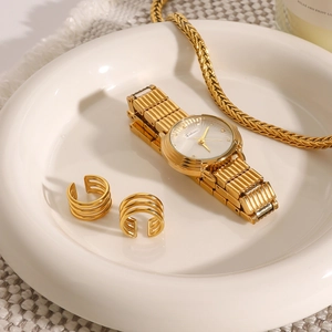 Golden watch and triple-layered ear cuff set displayed on white ceramic plate