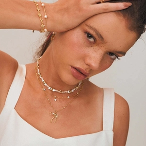 Detailed view of elegant gold layered necklace with pearl and bow charm on a model