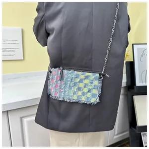 Detail of colorful plaid denim crossbody bag featuring frayed fringe texture and chain strap