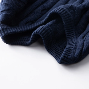 Detailed close-up of navy blue cable knit texture and ribbed hem on cotton sweater