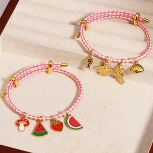 Adjustable woven rope bracelets with gold ocean and fruit charms on a beige velvet tray