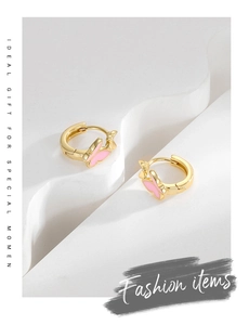 Detailed shot of gold butterfly earrings with pink enamel finish on white pedestal
