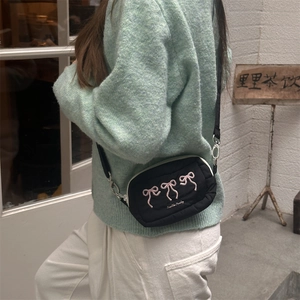 Close-up of black nylon crossbody bag featuring pink embroidered bows and zipper detail