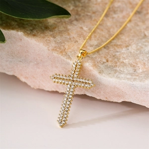 Macro d'un collier croix en or avec oxydes de zirconium sur un fond de pierre rose