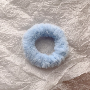 Macro detail of a soft light blue faux rabbit fur scrunchie on a white textured surface