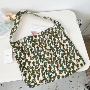 Flat lay of beige canvas tote bag with green floral pattern on a white desk surface