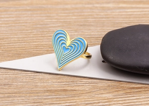 Detail of 18K gold plated heart ring with blue gradient enamel on a modern wooden background