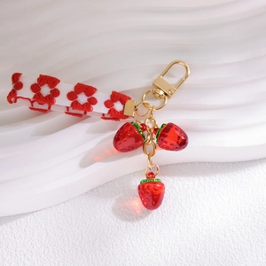 Detail of red crystal strawberry pendants on gold chain with white floral ribbon strap