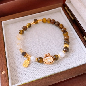 Dettaglio del bracciale in occhio di tigre e perle con un ciondolo a coniglio