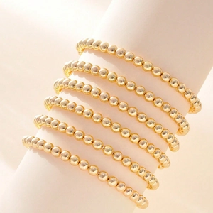 Detailed close-up of layered gold beaded elastic bracelets on a white cylinder stand