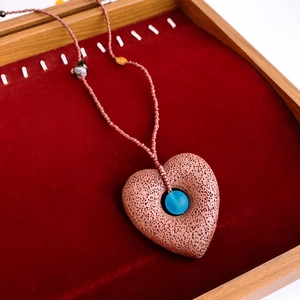 Detailed shot of heart-shaped volcanic stone pendant with blue bead on red velvet tray