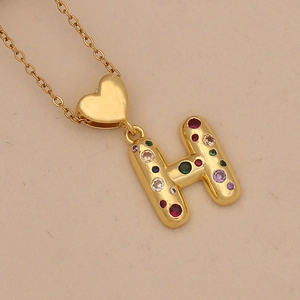Macro shot of gold letter H necklace with colorful cubic zirconia and heart link