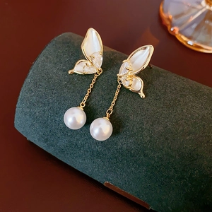 Macro shot of 14K gold plated butterfly earrings with hanging pearls on green velvet