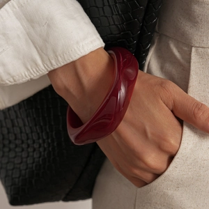 Détail d'un bracelet en acrylique torsadé rouge foncé translucide porté par un mannequin