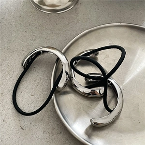 Close-up of minimalist silver metallic ponytail holders on a textured display tray