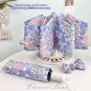 Close-up of purple floral folding umbrella with a matching bow tie accessory on white table