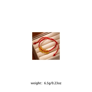 Detailed view of Red woven cord bracelet with golden coin charm on jewelry box padding