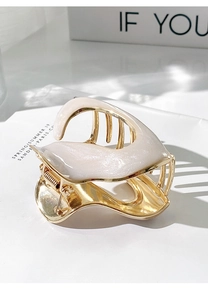 Close-up of cream dripping oil metal hair claw clip with gold accents on a magazine