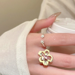 Detail of yellow enamel flower ring and silver ring set worn on hand holding a coffee cup