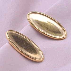 Macro shot of gold oval stainless steel earring studs on purple fabric background